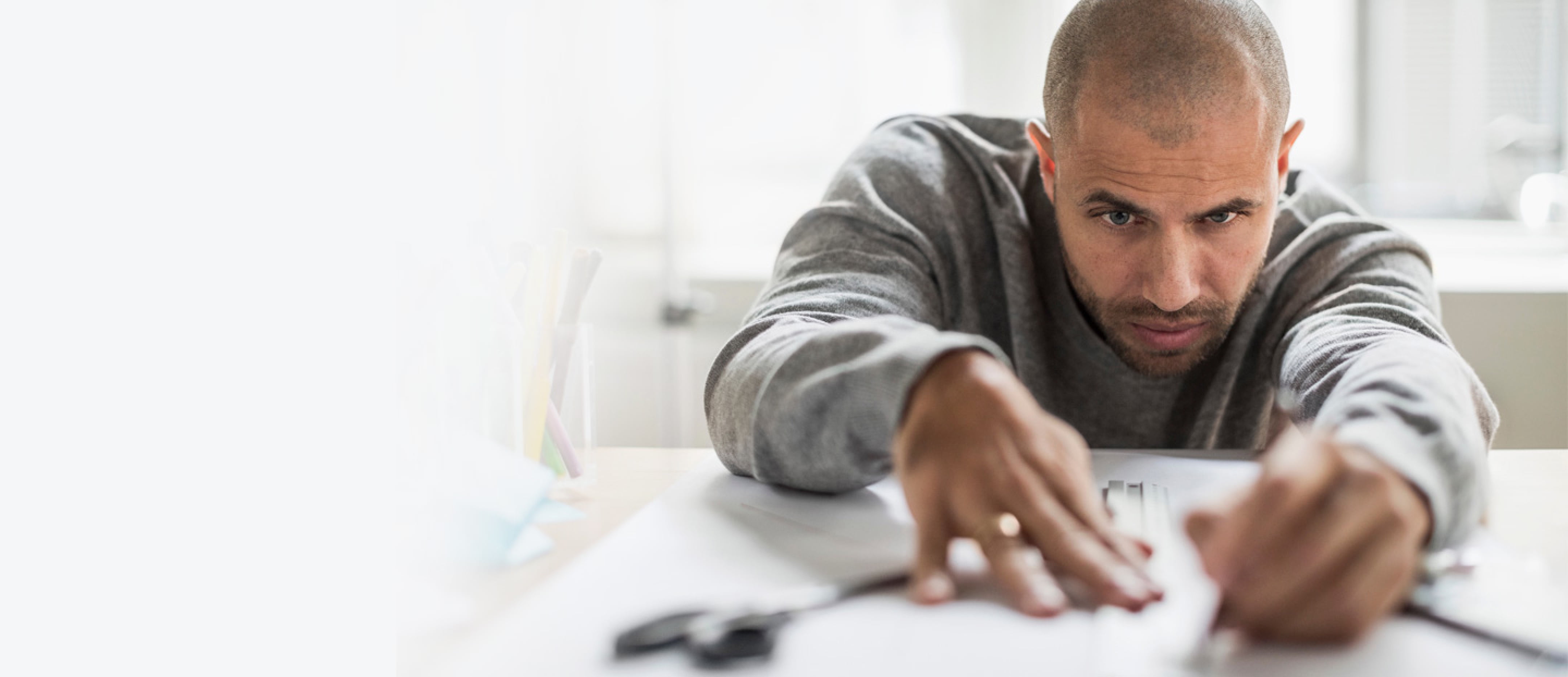 A man leans low over a table with a concentrated look, holding a pencil to paper.