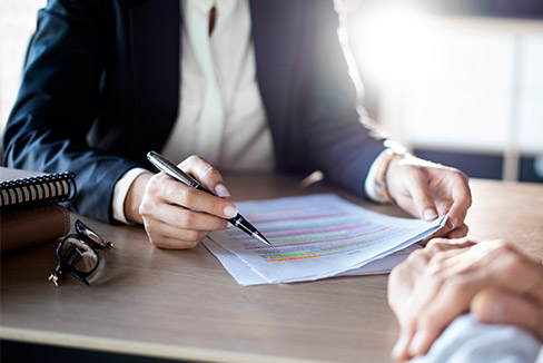 A woman's hands are seen as she scans a document that is highlighted in different colours. A man's hand rest on the desk opposite her.