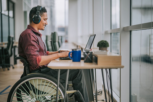 Asian indian male in a wheelchair sits at a desk on a video conference.